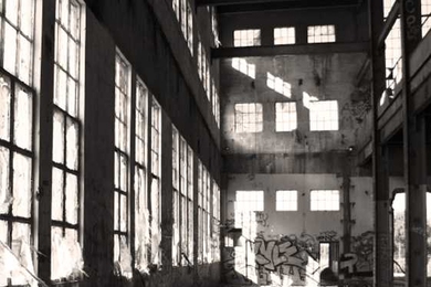 Nighttime black and white photo outside a warehouse where the lights are on, and the exterior wall has been marked with graffiti 