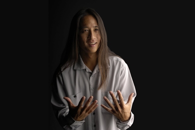 Photo of Kealoha Wong standing with his hands out in front of a black background 