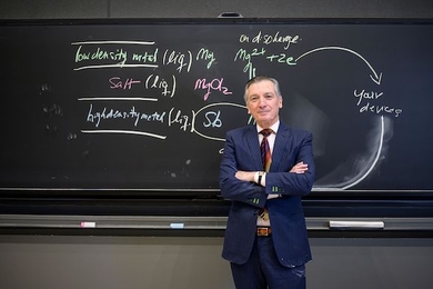 Donald Sadoway stands with his arms folded in front of a chalk board