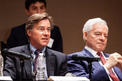 Robert Stoner speaks into a microphone with another man, out of focus, seated beside him.