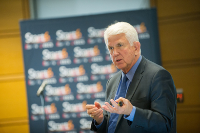 Bob Metcalfe speaks at an event, with blurry banner in background