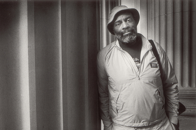 Black and white photo of Mel King leaning against large stone columns on the MIT campus