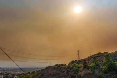 Photo of the sun peeking through orange smoggy air over a hillside, with Los Angeles in the background