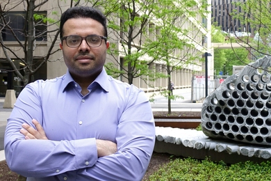 Soroush Mahjoubi stands in front of a concrete building and a concrete-based artwork that looks a bit like a giant honeycomb