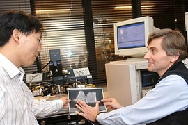Postdoctoral associate Dae-Hyun Kim, left, and Professor JesÃºs del Alamo look at a cross-section of the new transistor they have been developing. Behind them is the test equipment used to measure its characteristics.