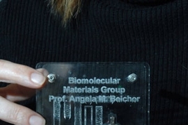 Angela Belcher holds a display of the virus-built battery she helped engineer. The battery --Â the silver-colored disc --Â is being used to power an LED.