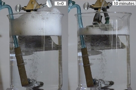 In a beaker with a constant stream of bubbles, inserting a piece of the new textured material developed by the MIT team (gray object extending into the surface at top) causes the foam buildup at the top of the beaker to dissipate almost completely within ten minutes.