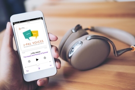 Photo of a hand holding a smartphone with headphones in the background