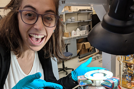 Photo of Chiara Salemi with blue latex gloves pointing at the ABRACADABRA toroid magnet