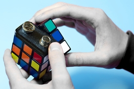 Conceptual photo featuring two hands, each turning a section of a battery that looks like a Rubick's cube