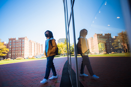Photo of a student wearing a mask, walking next to MIT's Kresge auditorium