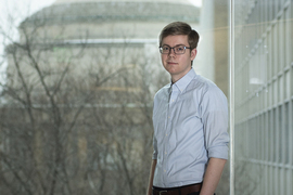 Photo of Connor Coley standing in front of a window with the MIT Dome in the background