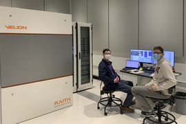 Photo of two masked researchers using the VELION, which is in a large beige metal cabinet, at MIT.nano