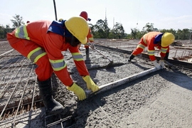 Photo of three workers in orange jumpsuits and yellow hard hats laying concrete.