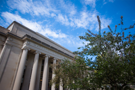 Photo of the facade of MIT Building 10, featuring ionic columns, as well as a tree with green leaves