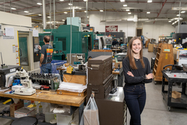 Portrait of Caitlin Braun posing in a large lab space with many tables and pieces of technical equipment