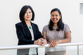 Portrait photo of Lisa Yang and Ila Fiete standing next to one another with their folded hands resting on a railing