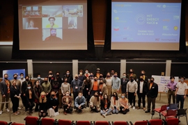 Photo of at least 3 dozen people posing on a stage. All are wearing face masks.