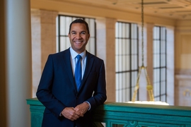 Photo of John Dozier in a suit and tie, smiling and leaning on a railing