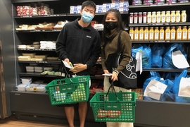 Photo of two students at a supermarket, posing with a basket of grocery items.