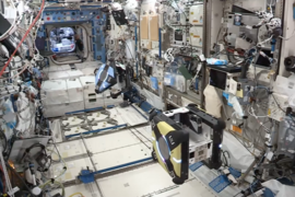 Photo of the interior of International Space Station with two robots floating in the middle