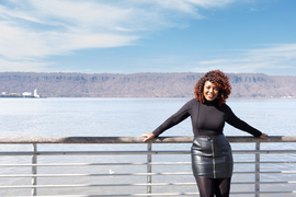 Portrait of Janelle Heslop leaning against a railing with a body of water in the background