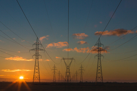 Photo of the sun setting behind some power grid lines