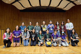 17 girls pose with their trophies on a stage at MIT