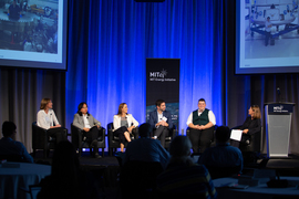 Five panelists sit in a row on stage with a moderator.