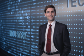 Tomás Palacios stands in front of a large blue screen which reads "Industry”.