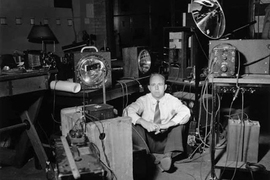 Historical black-and-white photo of Harold “Doc” Edgerton sitting on the floor in a room surrounded by strobe lights.