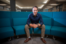 Jason Jay sits on a curved blue sectional couch inside an office