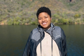 Elissa Gibson standing in front of a lake. She is smiling and wearing binoculars around her neck.