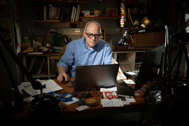 Danny Braunstein, sitting in a pool of light in an otherwise-dim room, looks at a laptop. There is a professional-grade boom microphone in front of him.