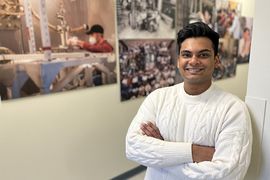Student in white sweater, arms crossed, in front of picture wall in hallway