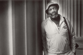Black and white photo of Mel King leaning against large stone columns on the MIT campus