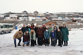 15 students and faculty pose for a group photo in front of snow-dusted residential gers