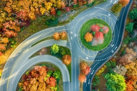 Aerial overhead view of several roadways converging into and separating out from a rotary amidst fall foliage.