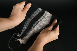 2 hands pull and stretch a piece of black and white fabric that has been sewn using the new fiber.