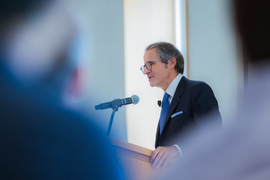 Rafael Mariano Grossi speaks at a lectern, framed by out-of-focus audience members in the foreground
