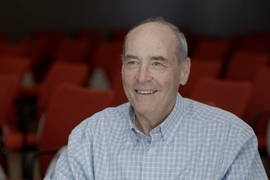 Mark Bear is sitting in an auditorium full of red chairs and smiling.