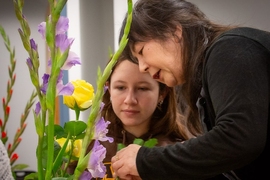 Hiroko Matsuyama works with a student to help arrange her flowers. The flowers are purple and yellow.