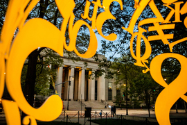 A view of the steps and columns of 77 Mass Ave, as seen through The Alchemist Sculpture. Glimpses of the numbers and mathematical symbols are seen around the image.