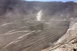 A copper mining pit dug deep in the ground, surrounded by grooved rings of rock and flying dust.