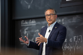 Ani Dasgupta gestures with his hands as he speaks while standing in front of chalkboard.