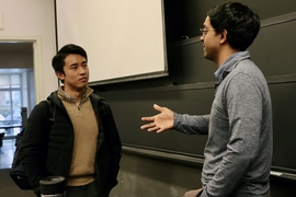 Ashesh Rambachan converses with a student in the front of a classroom.