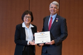 Heidi Shyu and Eric Evans stand side-by-side holding up a plaque between them. Evans has a medal pinned to his lapel.