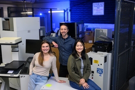 Anastasia Dunca, Chris Rabe, and Jasmin Liu stand in an electronic waste collection area, surrounded by electronic and lab equipment