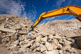 A crane arm hovers over large hills of construction debris on a sunny day