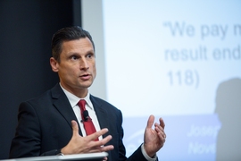 Joseph DeCarolis gestures with both hands while speaking at a lectern 
